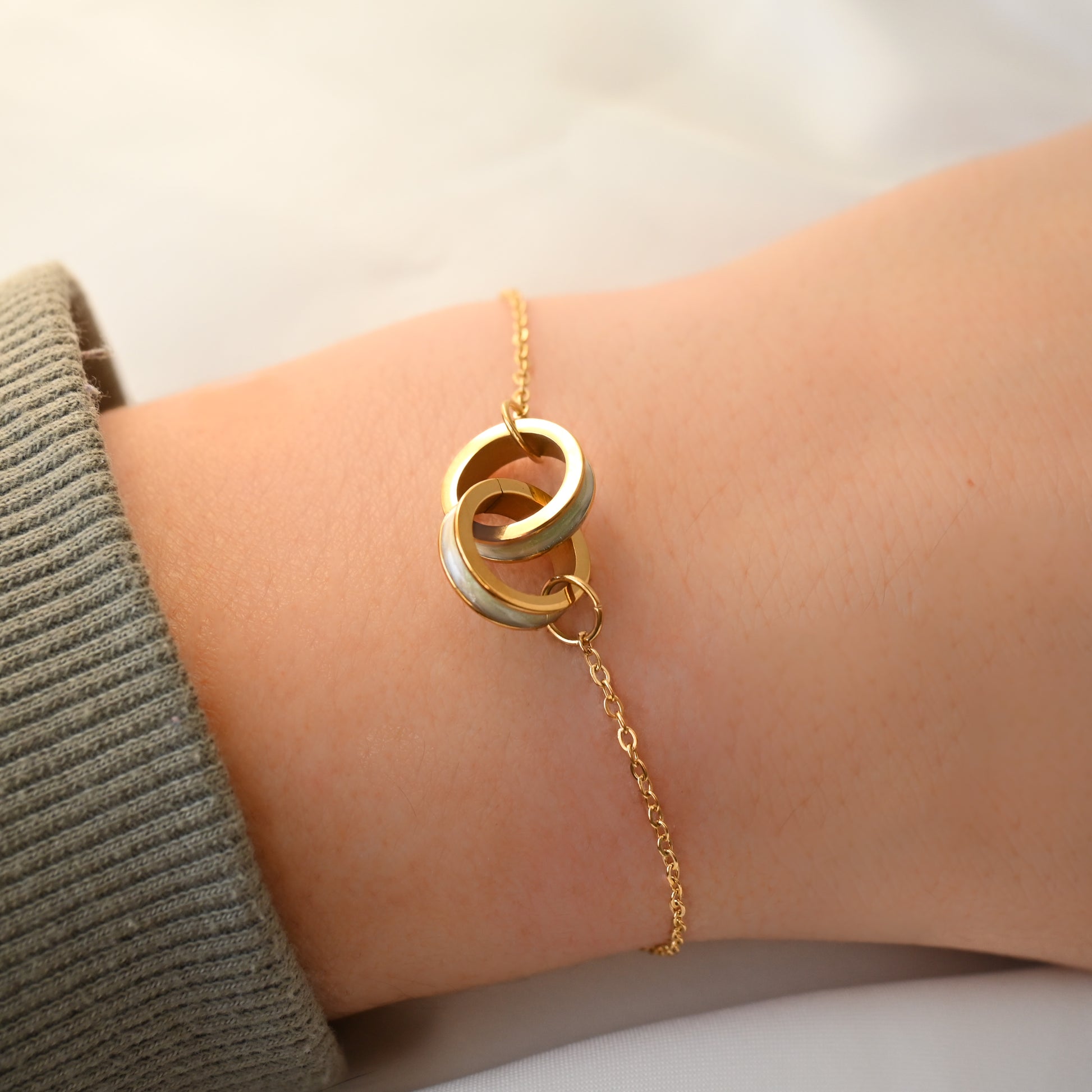 Gold chain bracelet with double rings on a wrist against a neutral background