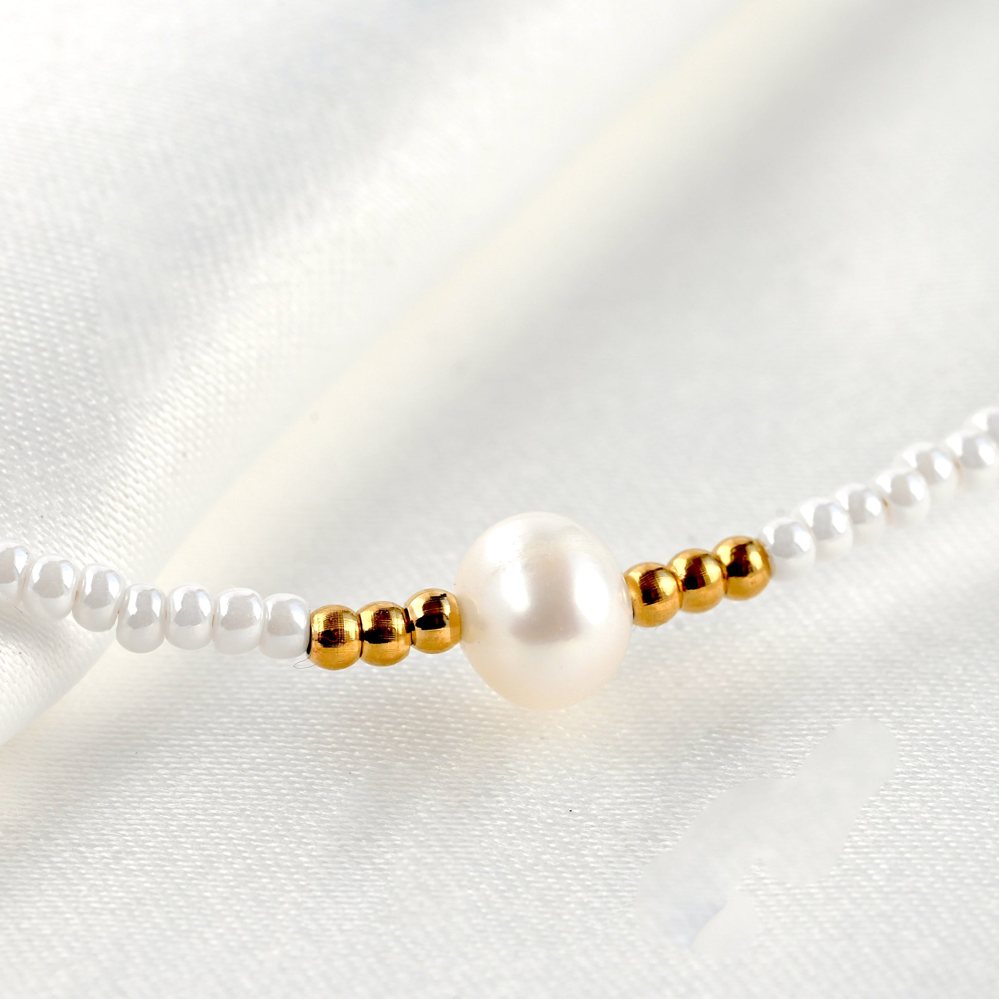 Close up view of the freshwater pearl and and 3 gold beads on each side and white seed beads all around on a white satin background