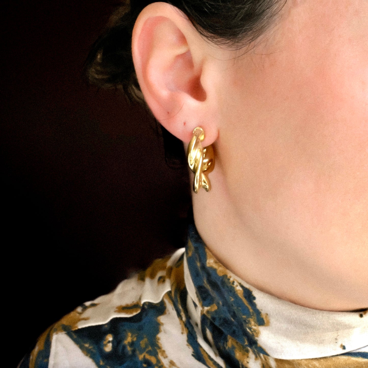 front view of gold hoop earrings worn by a person with a dark background