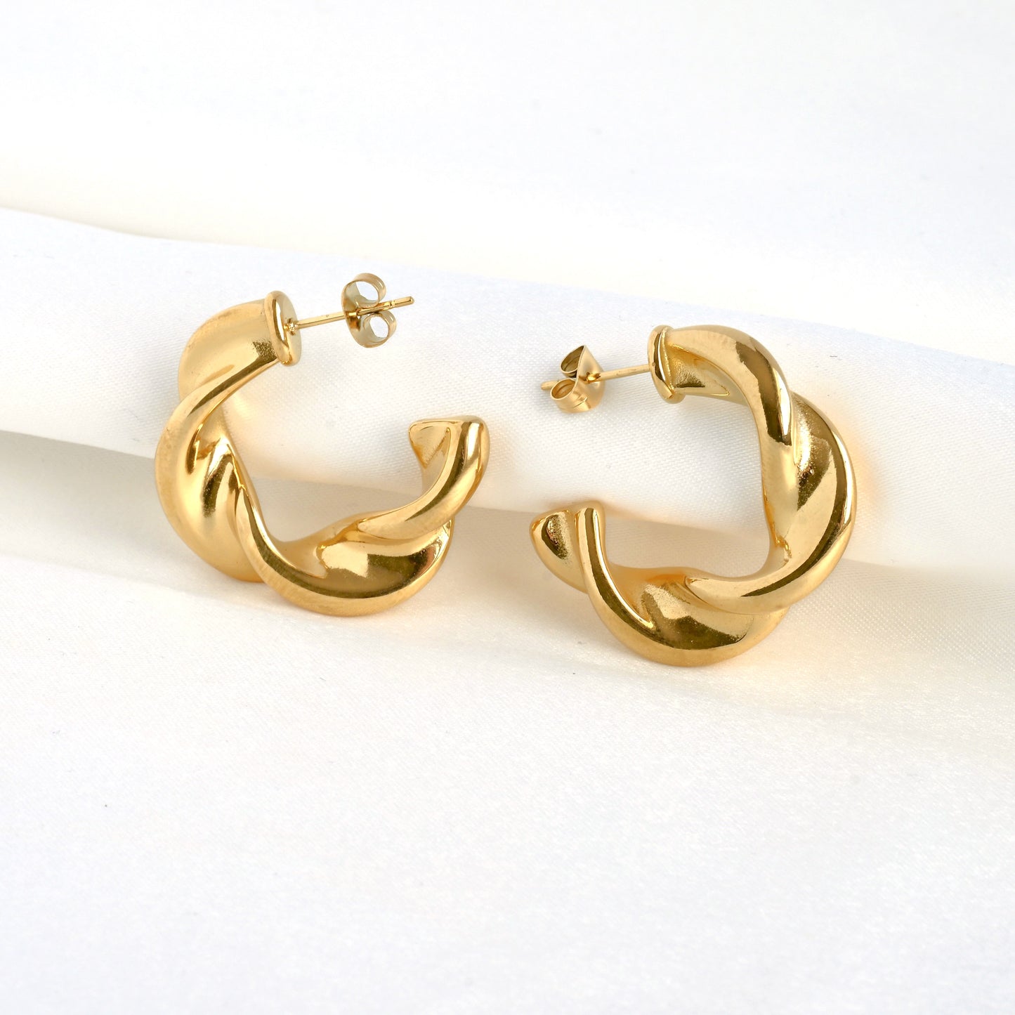 Gold C hoop earrrings against folded white satin fabric