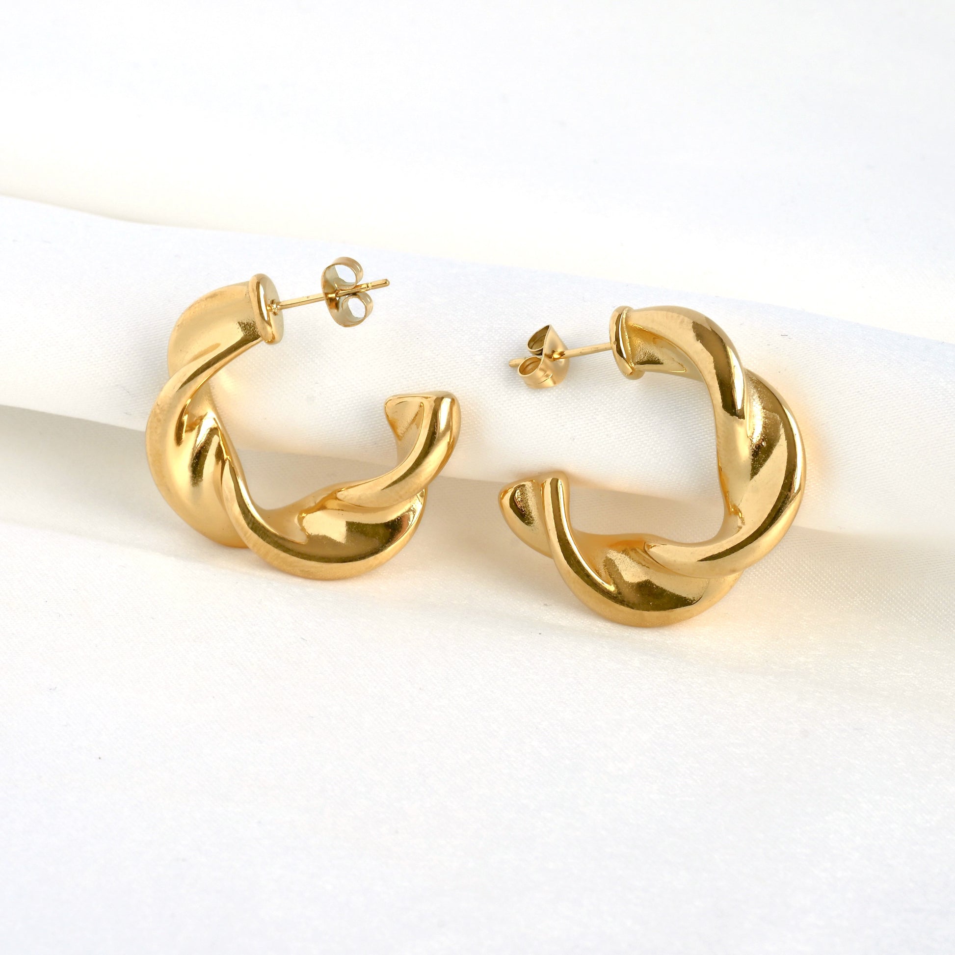 Gold C hoop earrrings against folded white satin fabric
