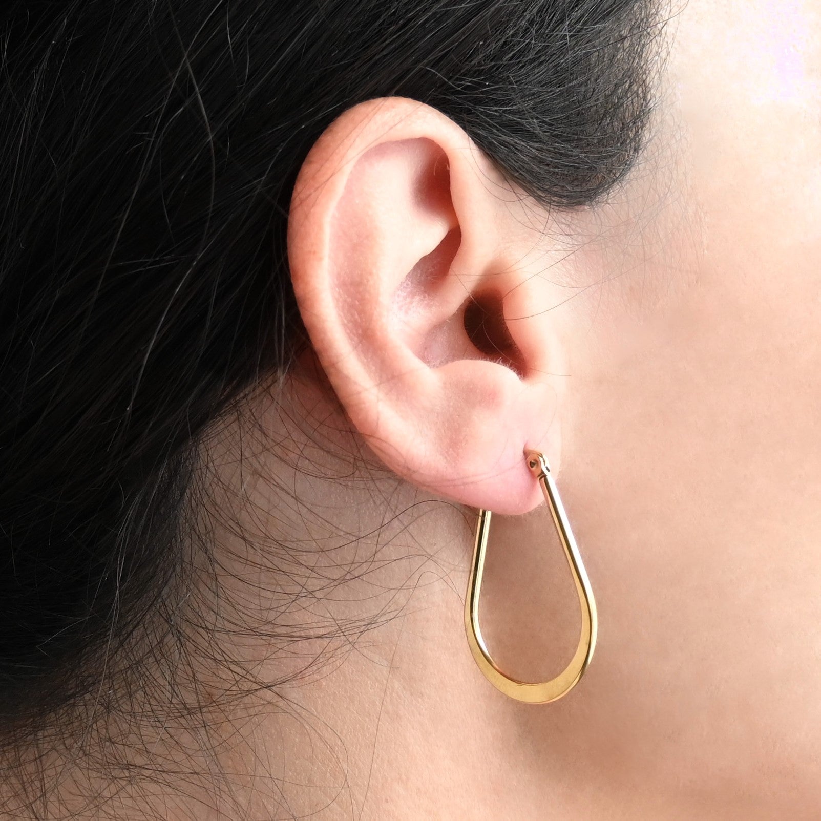 Side view of gold pear hoop earrings worn by a person with dark hair.