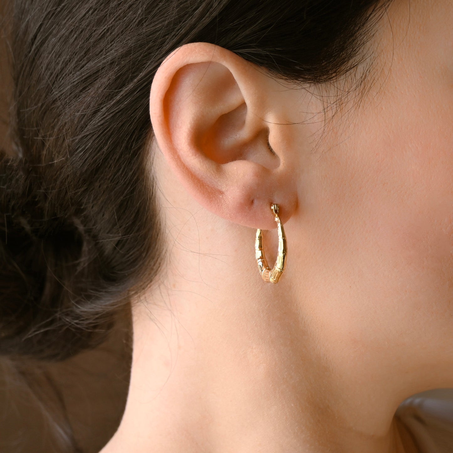 A close-up of a person's ear wearing a medium textured gold hoop earring.