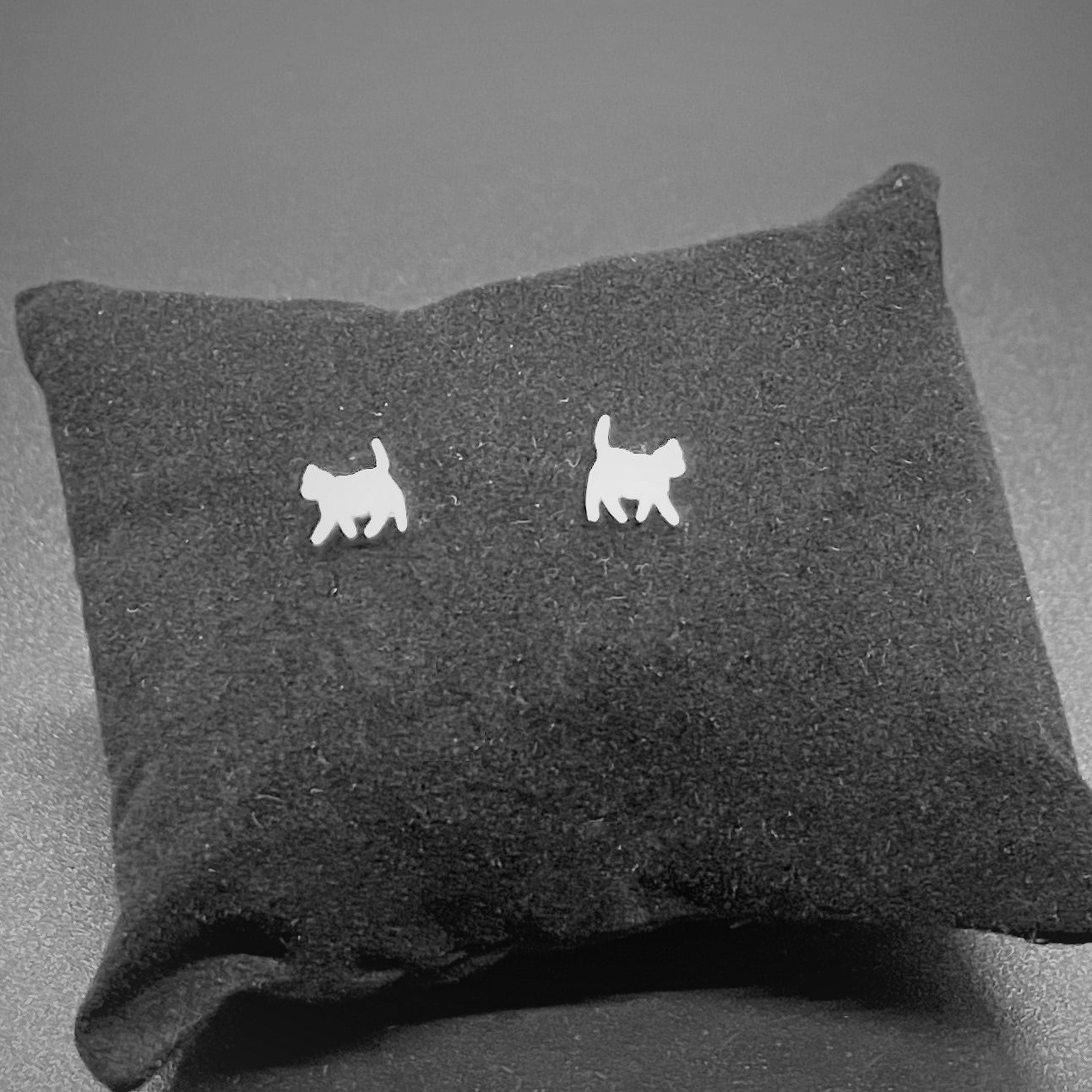 Cat stud earrings in silver on a black cushion against a gray background