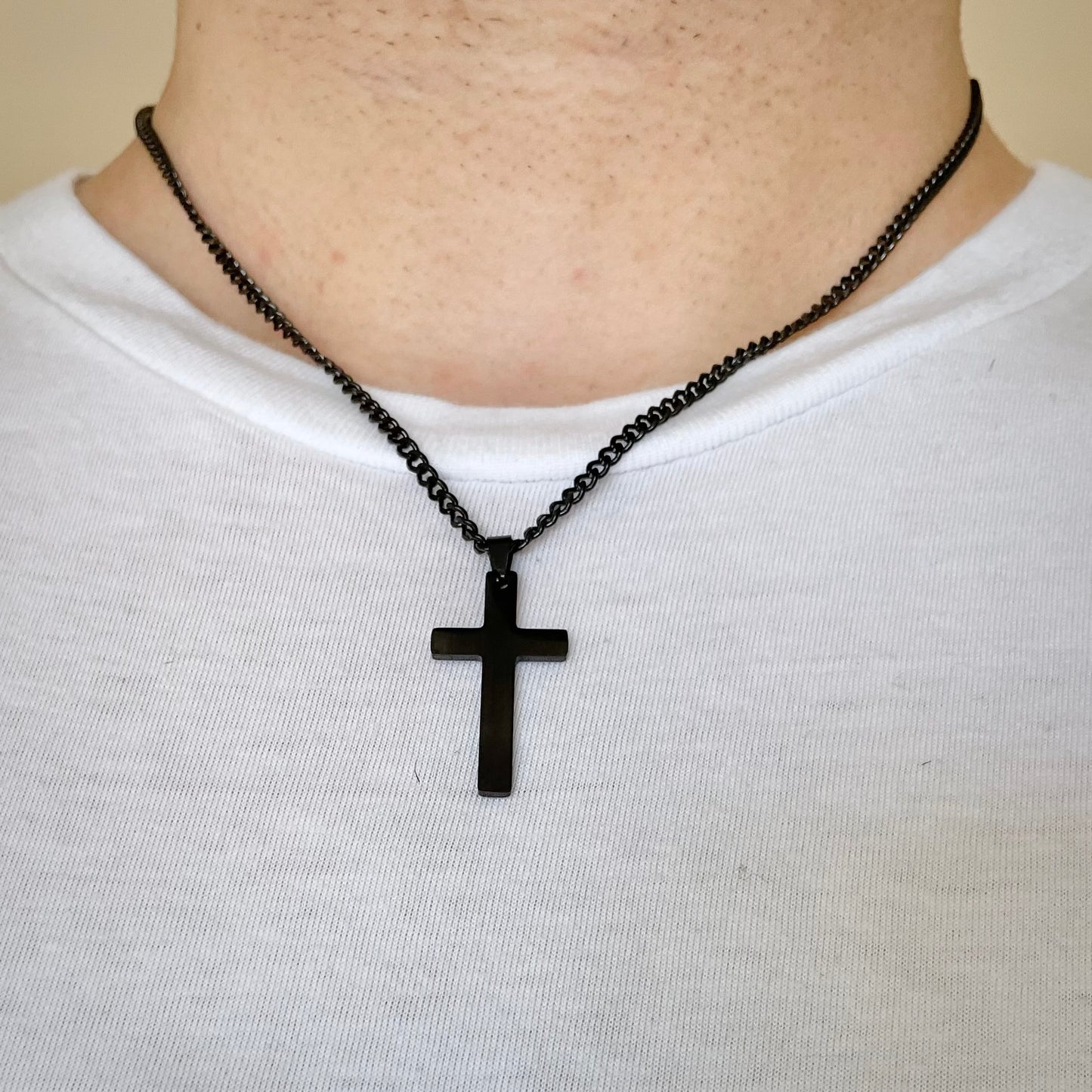 Black cross necklace with a curb chain on a person wearing a white shirt