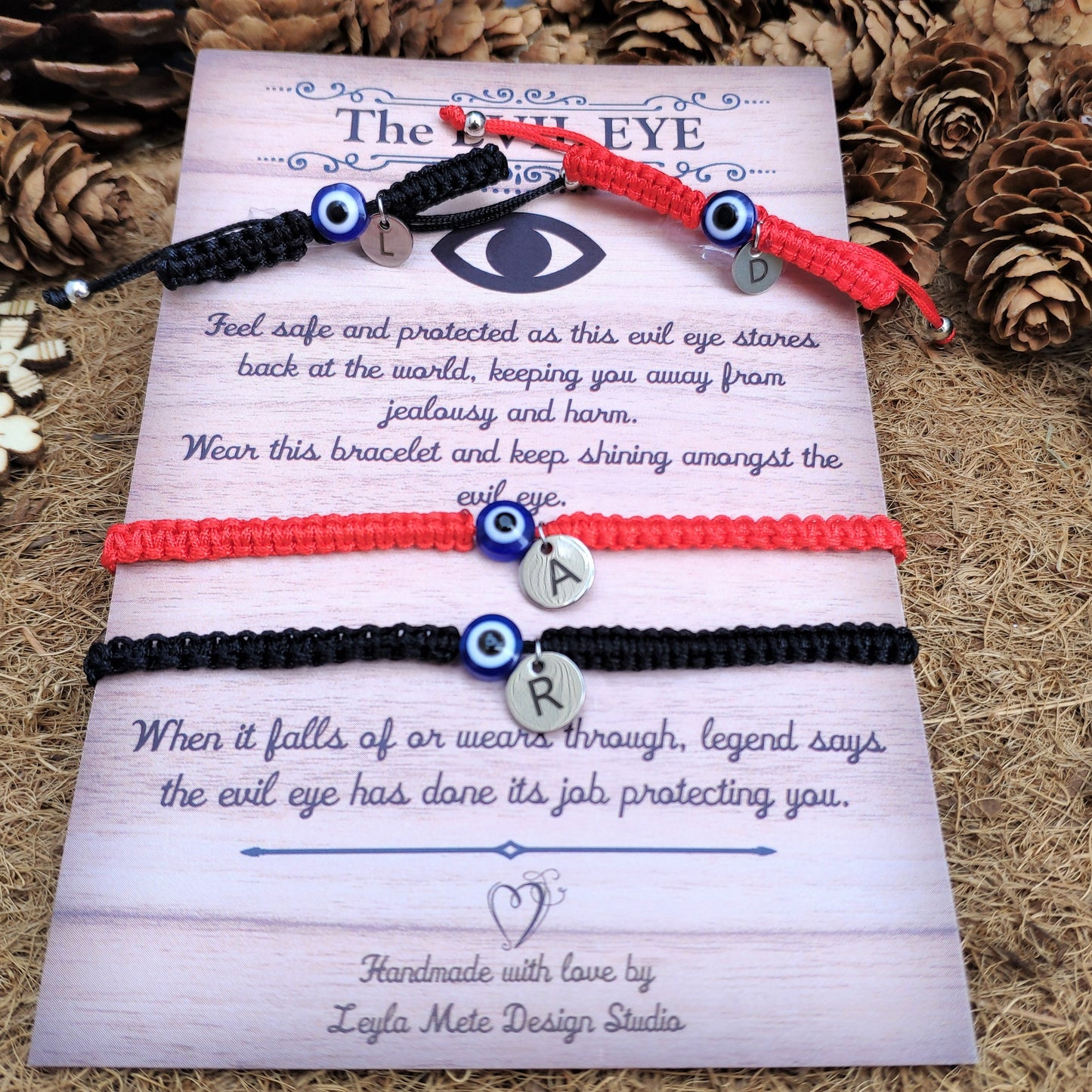 Two bracelets with evil eye charms on a decorative card with text, surrounded by pine cones and flowers.