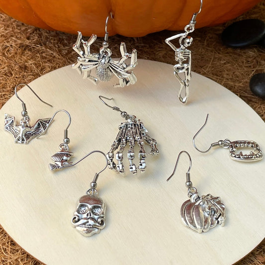 Collection of Halloween-themed silver earrings on a white plate with a pumpkin in the background.