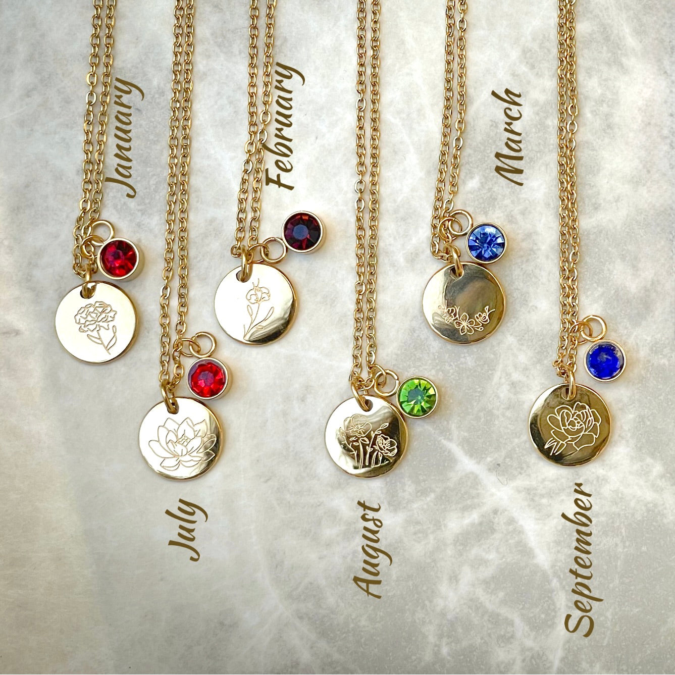 Gold flower necklaces with birthstone charms on a textured gray background