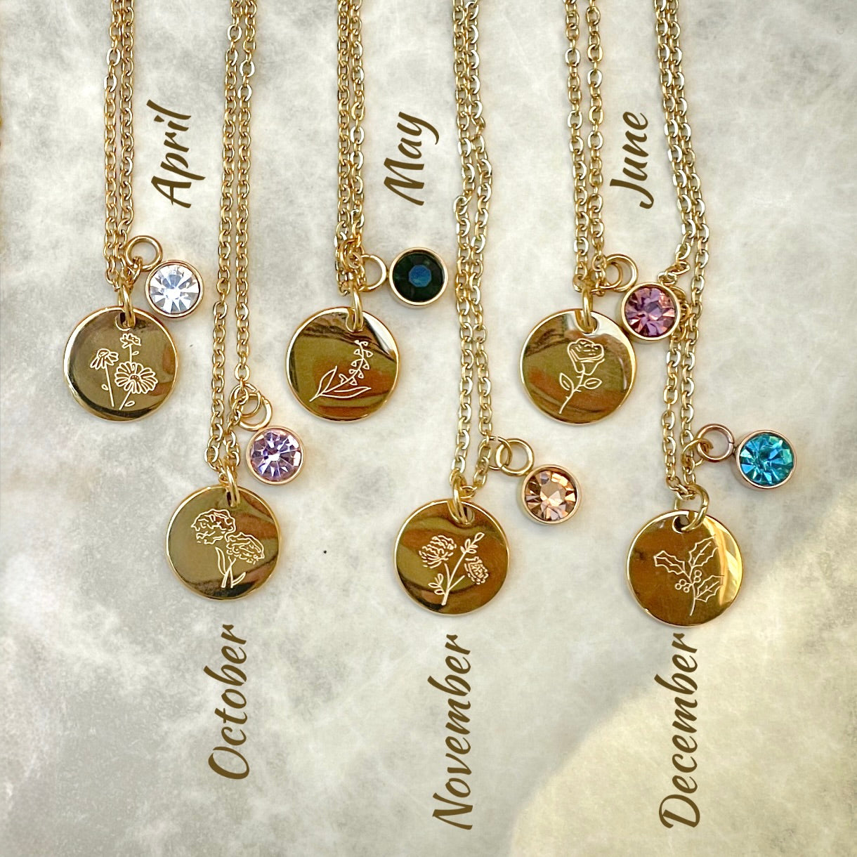 Birth flower engraved gold necklaces with birthstone charms on a textured surface
