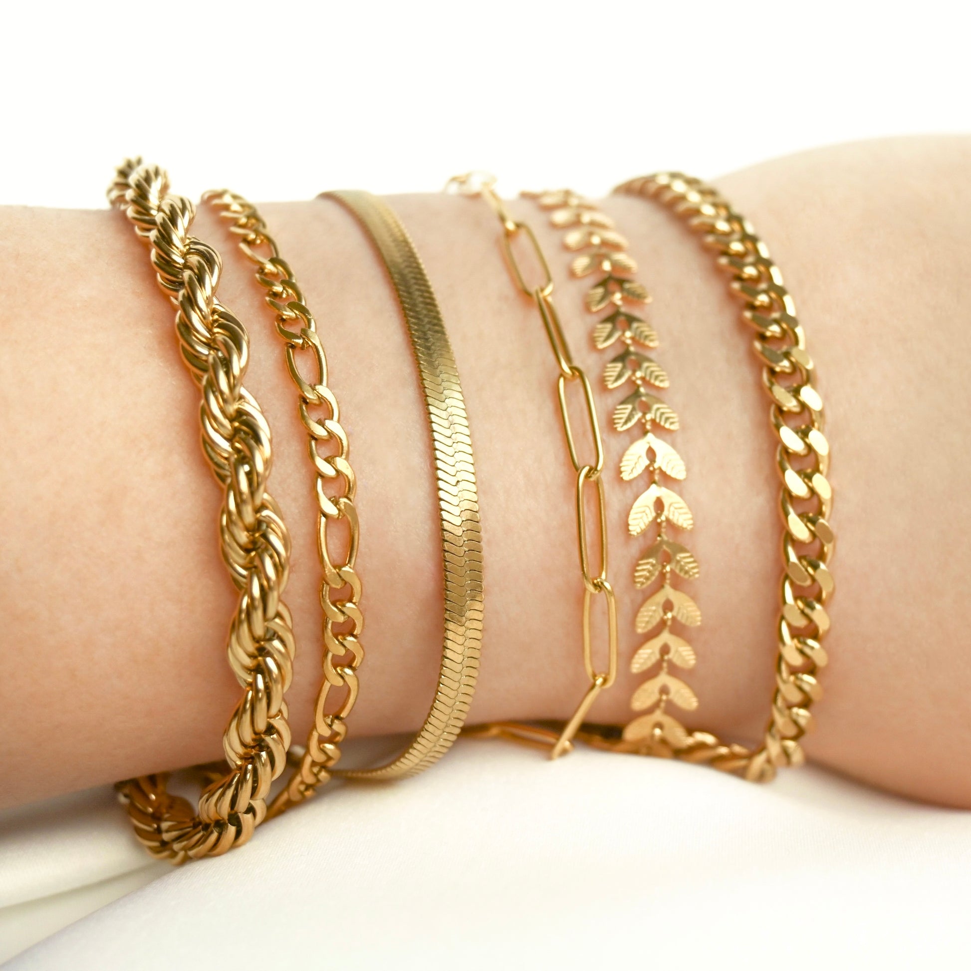 Collection of bold gold bracelets on a wrist against a white background