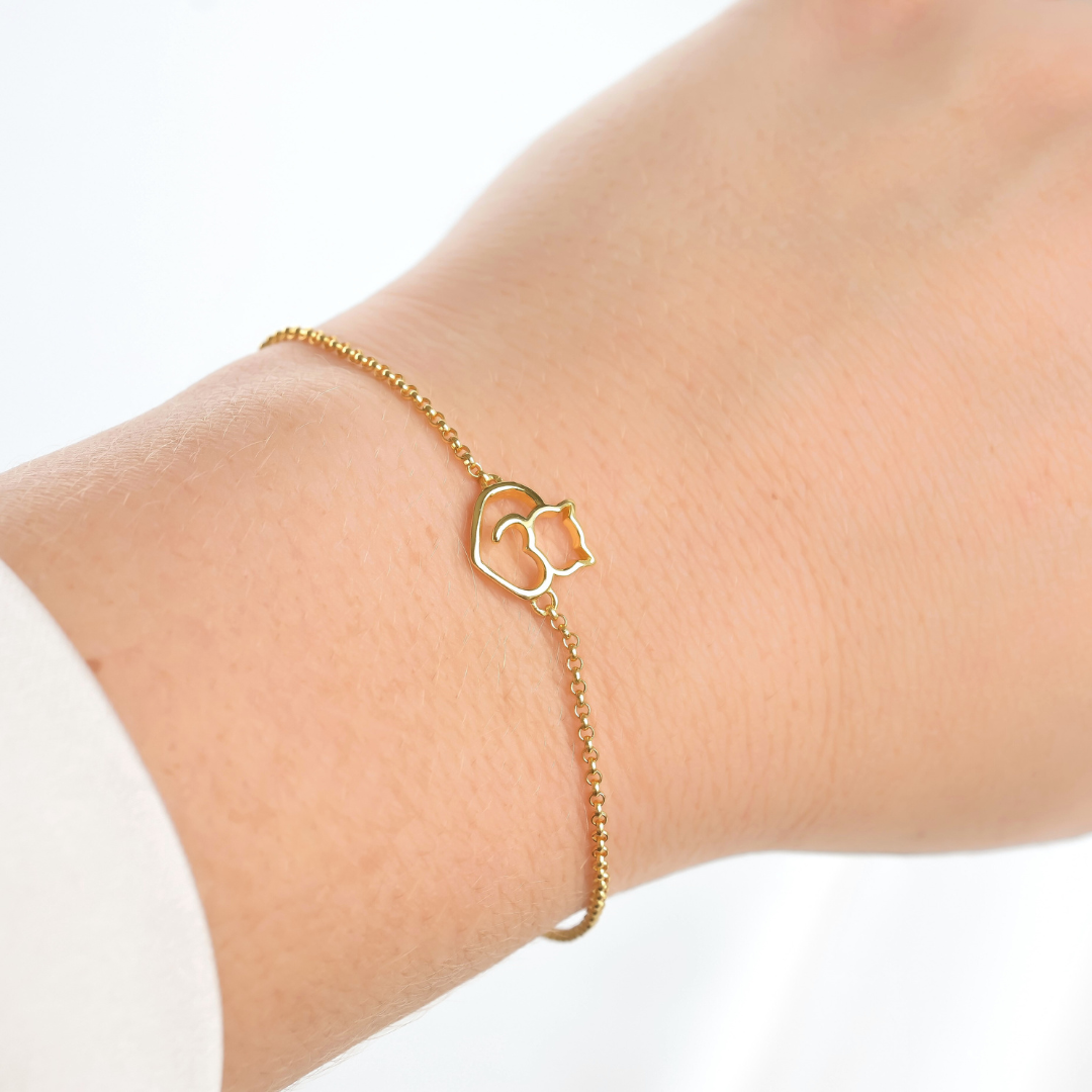 Gold bracelet with a cat heart charm on a wrist against a white background
