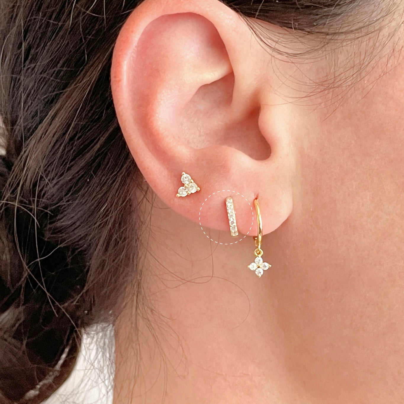 Close-up of an ear wearing gold earring stack  with half eternity pave cz design highlghted with white dotted circle