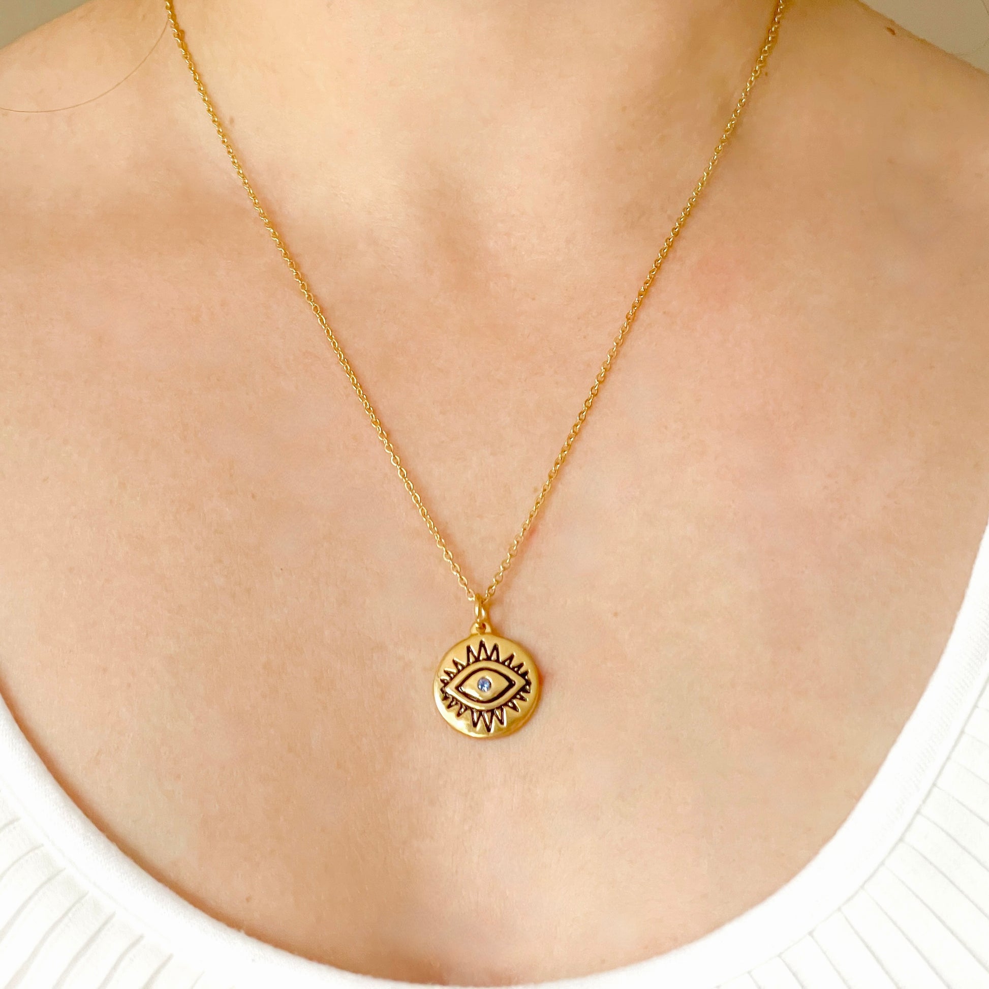Gold eye necklace with a round pendant featuring a black eye design on a person's neck.