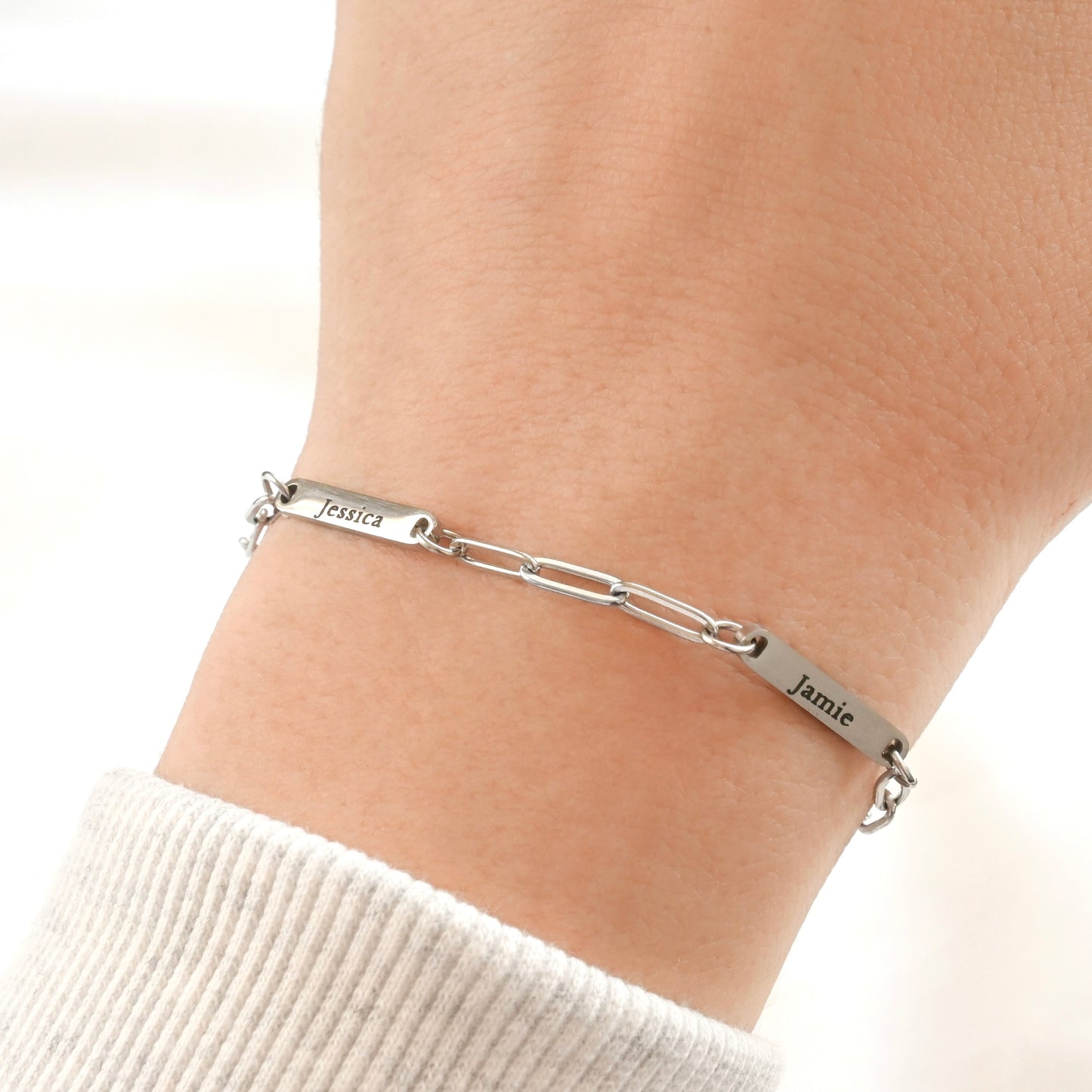Silver paperclip bracelet with engraved names on a wrist against a white background