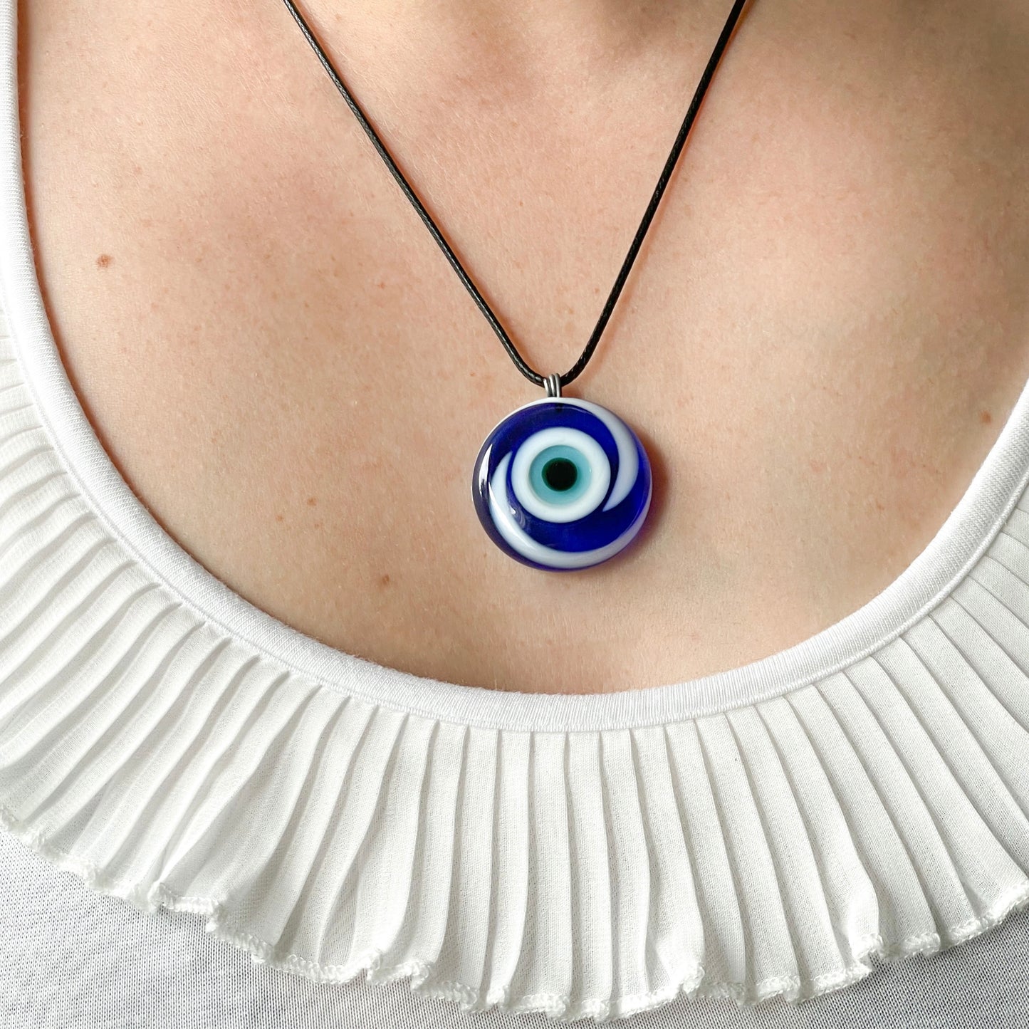 Necklace with a blue and white eye pendant worn by a person wearing a white top.