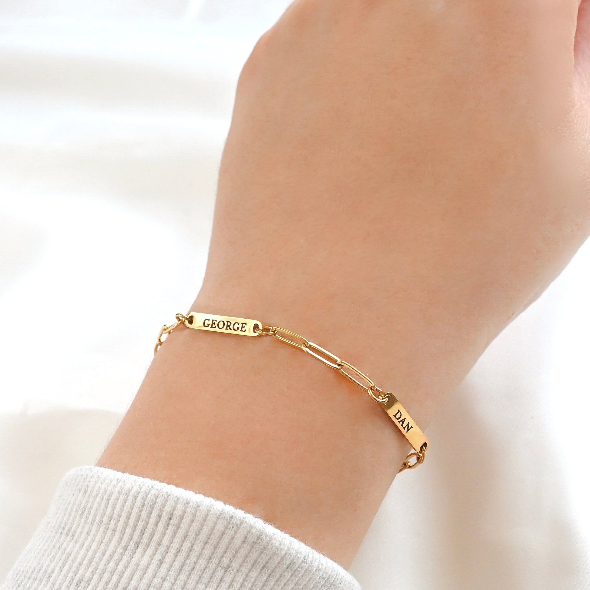Gold name bar bracelet on a wrist against a white background