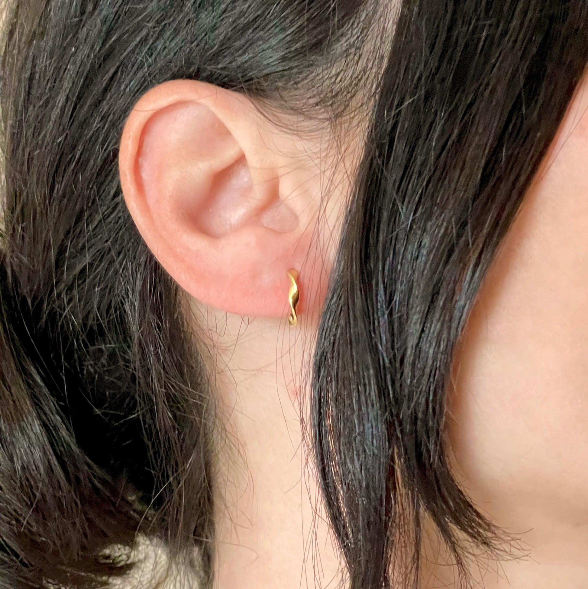 Small gold twisted hoops worn by a woman with dark hair.