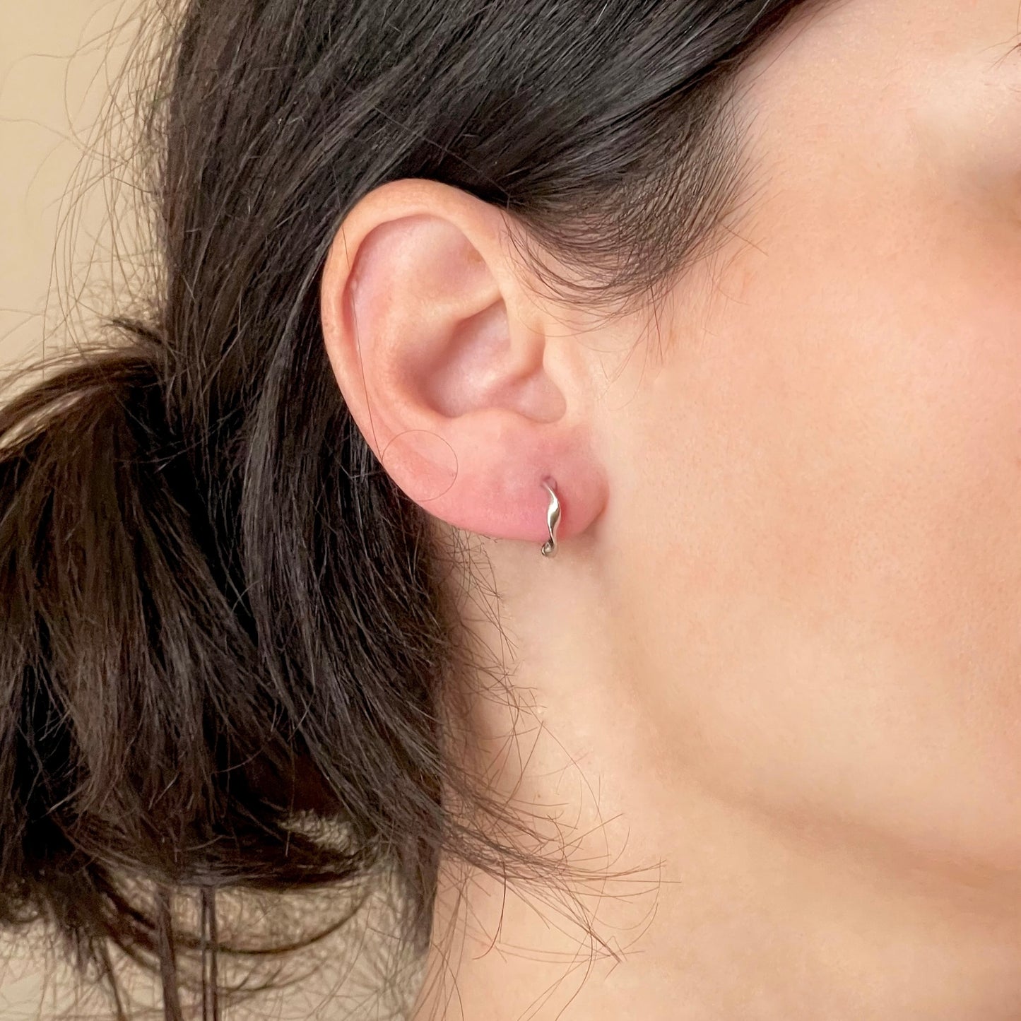 Close-up of an ear wearing a small vintage style twisted hoop earring with dark hair and blurred background