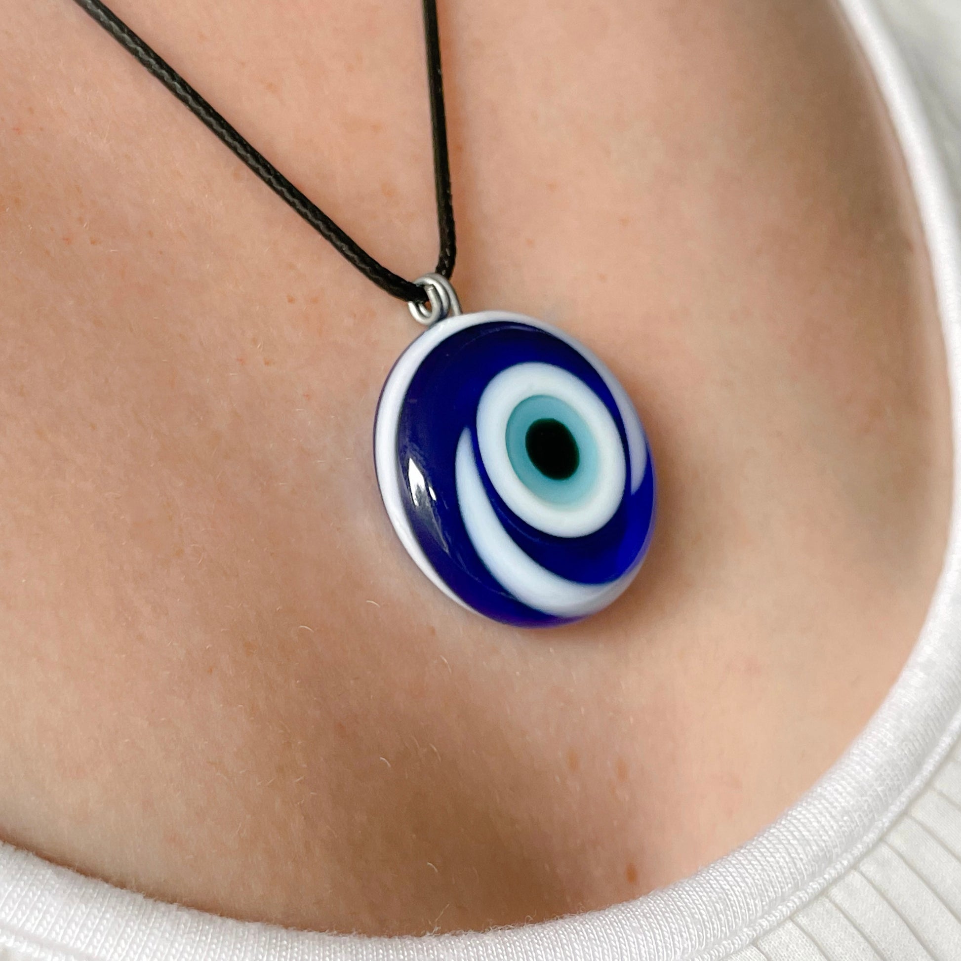 Close up view of blue evil eye medallion with a white swirl,  worn on a person's neck with a black cord