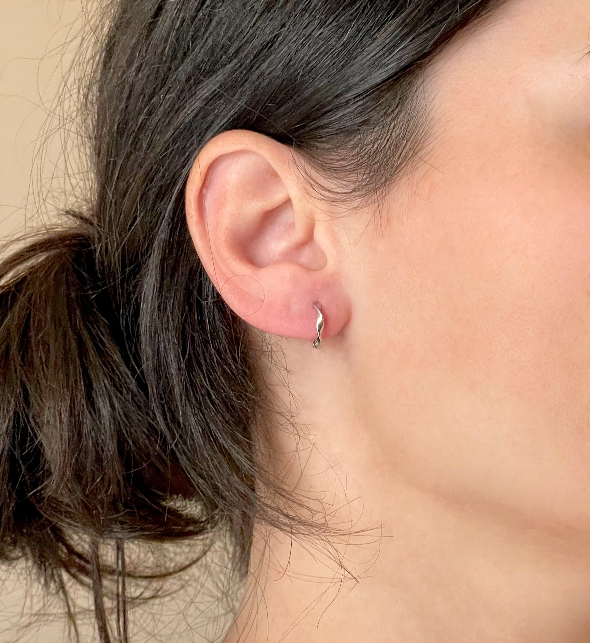 Twisted silver huggie earrings worn by a person