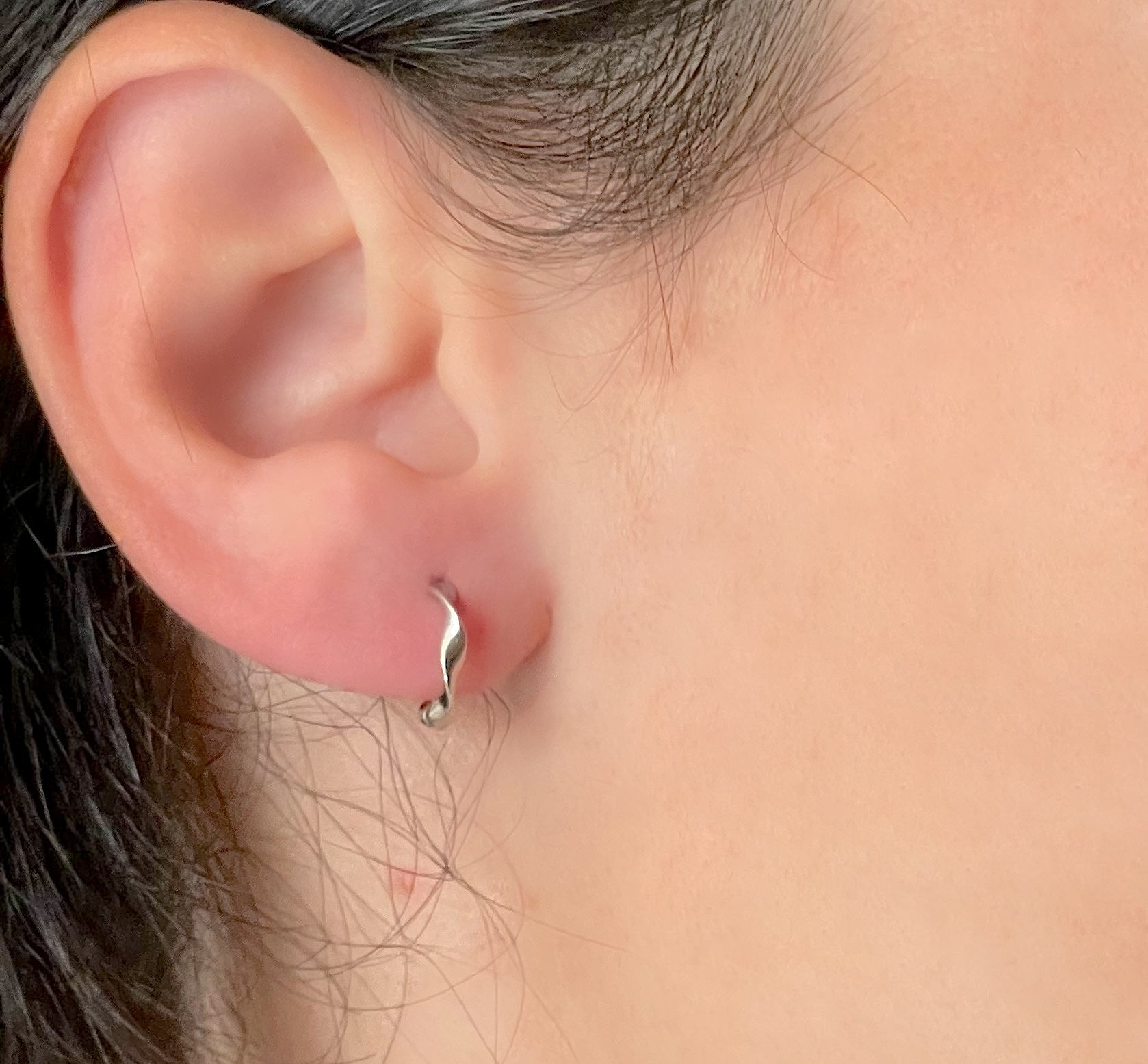 Close-up of an ear wearing silver hoop earrings with a swirling pattern, with a blurred background