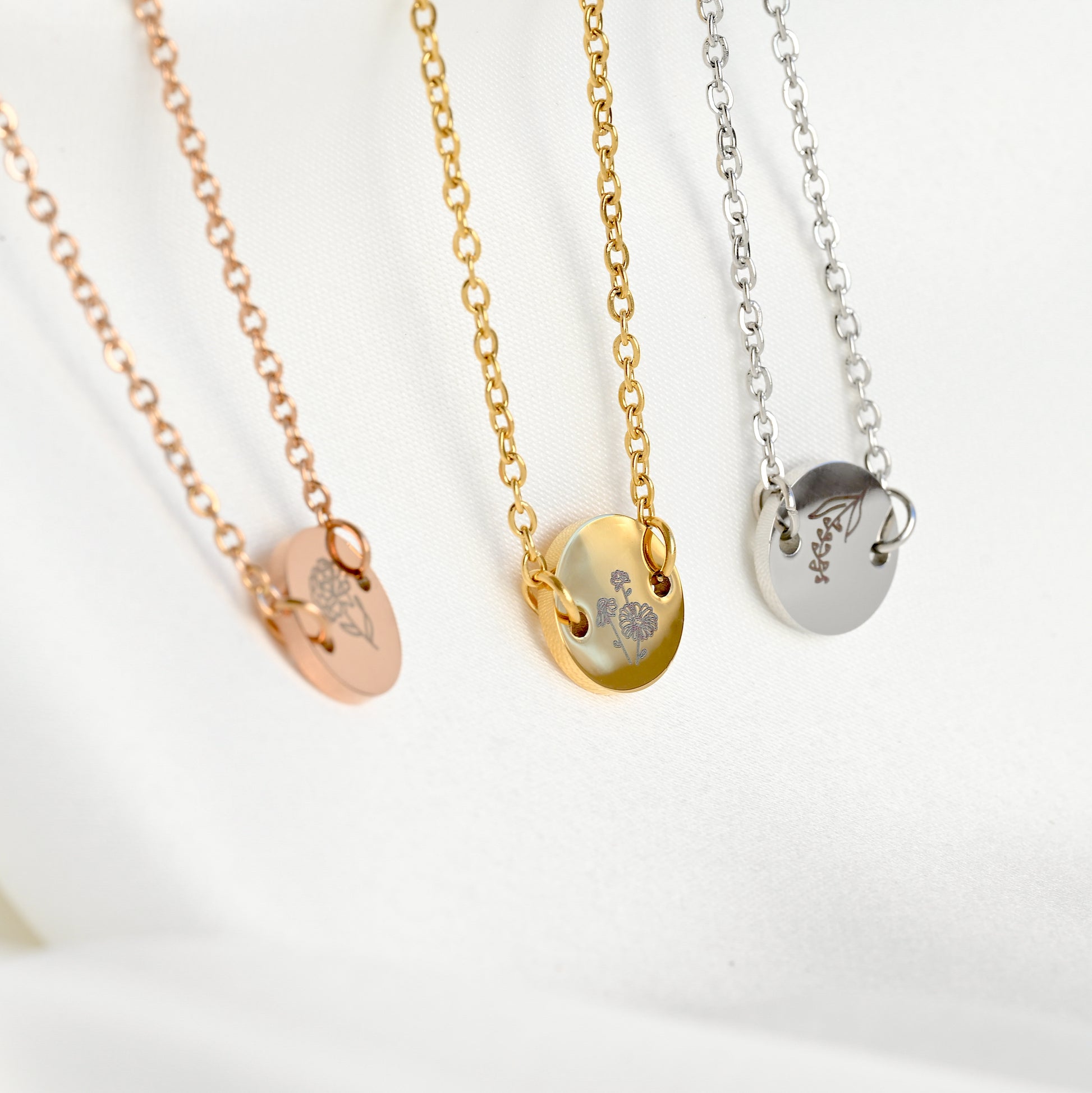 Side view of the rose gold, gold and silver bracelets with engraved birth flowers, showcasing the thickness of the coin charm on a white background