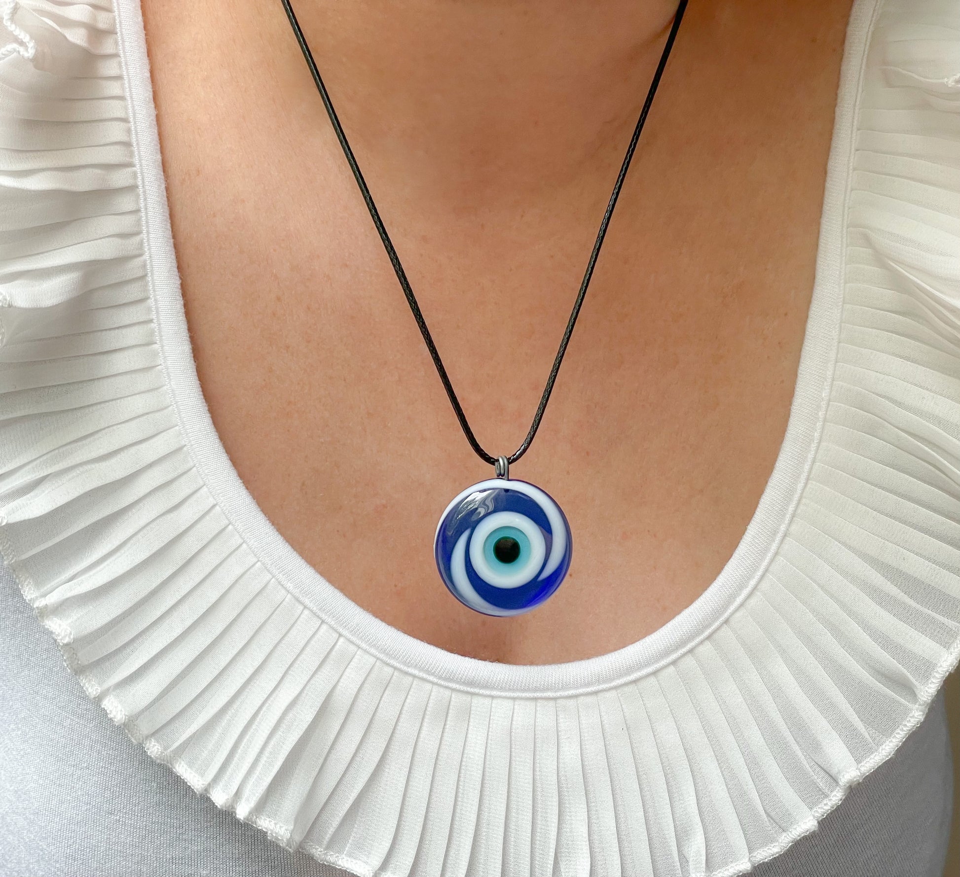 Necklace with a blue and white evil eye pendant worn by a person in a white top.