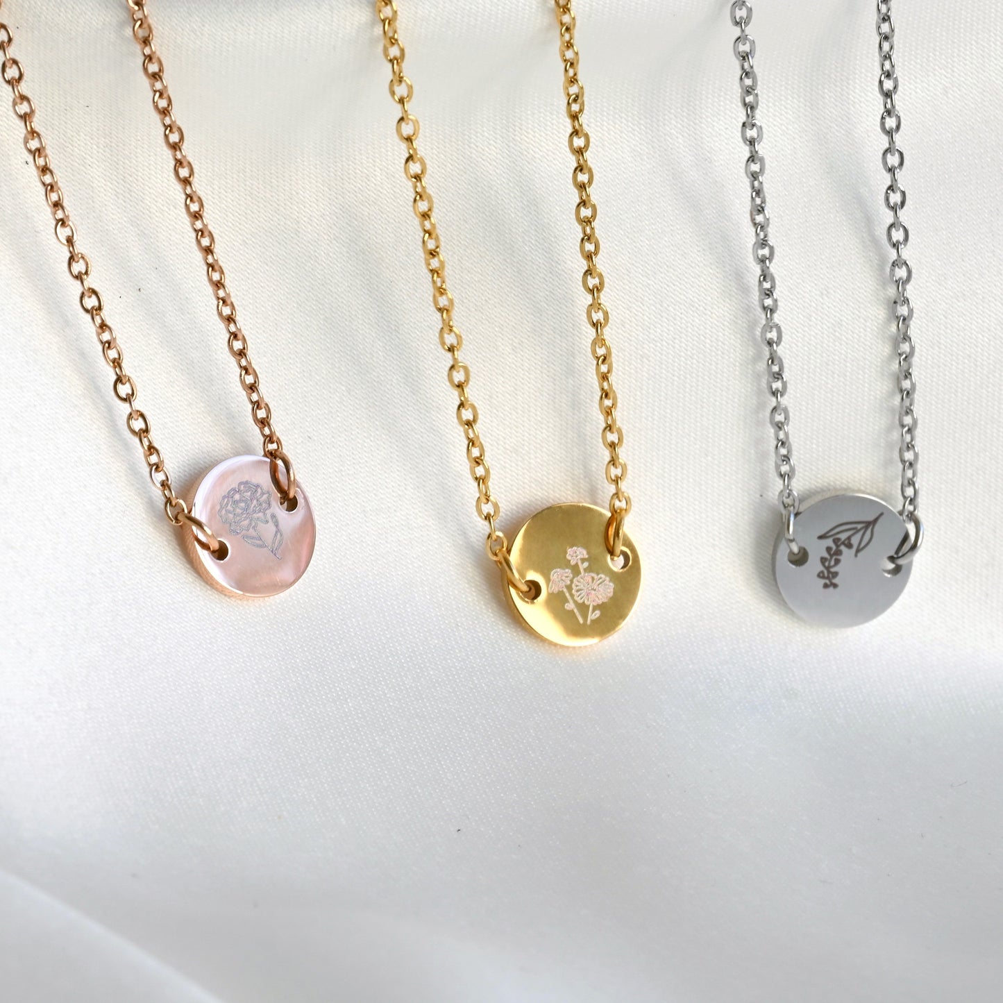 Three bracelet with circular flower pendants in rose gold, gold and silver from left to right, on a white background