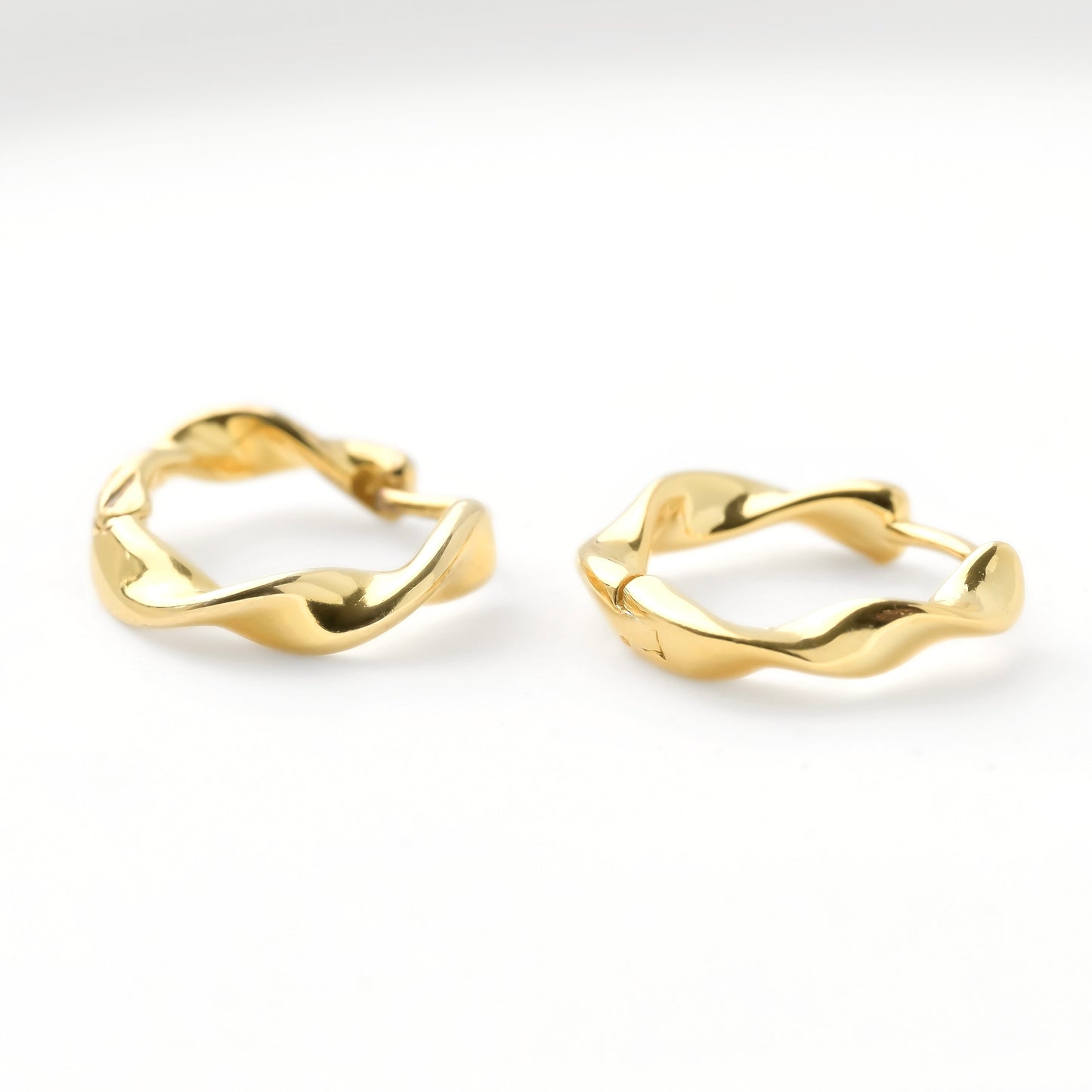 Twisted wavy gold huggie earrings on a white background