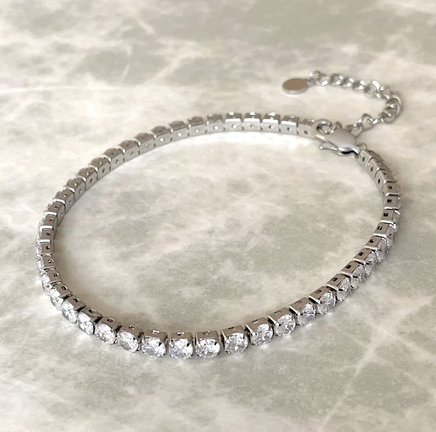 Silver tennis anklet with clear stones on a marble surface