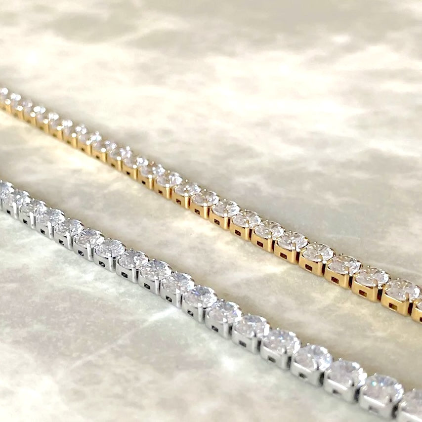 Two diamond tennis bracelets, one gold and one silver, on a light background.