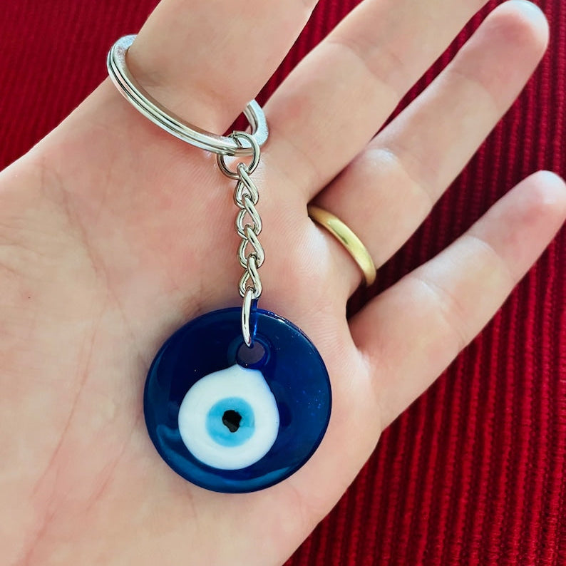 Hand holding a an evil eye keychain against a red background