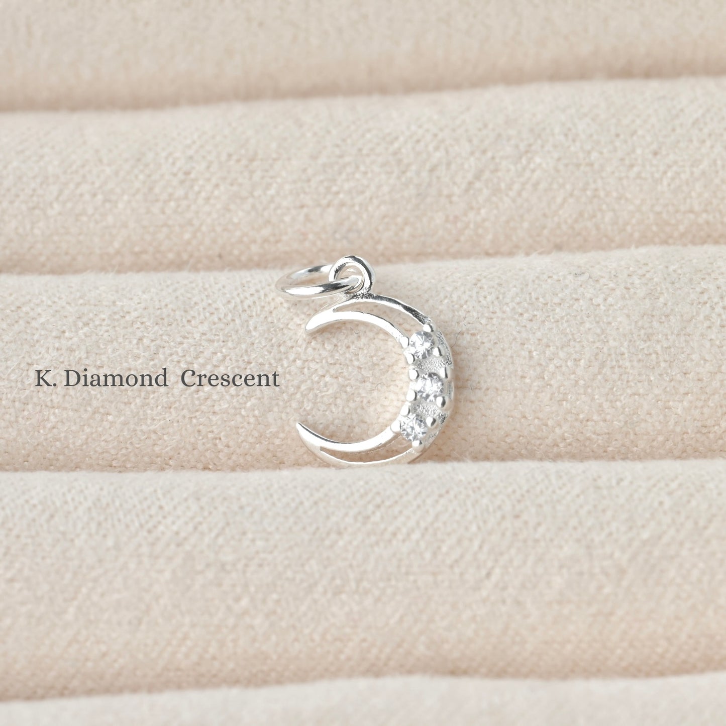 Silver crescent moon pendant with three embedded diamonds on a beige fabric background