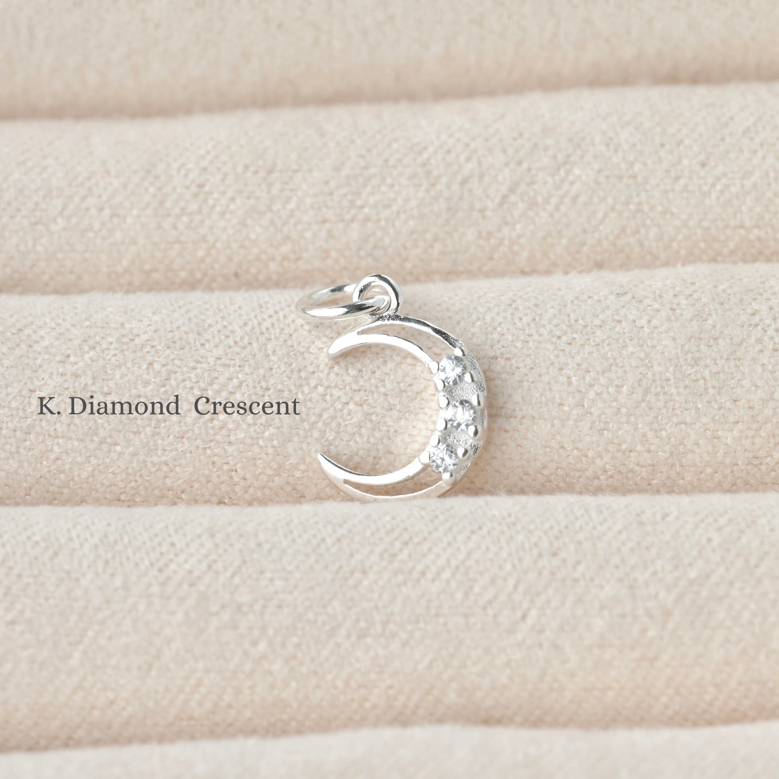 Silver crescent moon pendant with three embedded diamonds on a beige fabric background