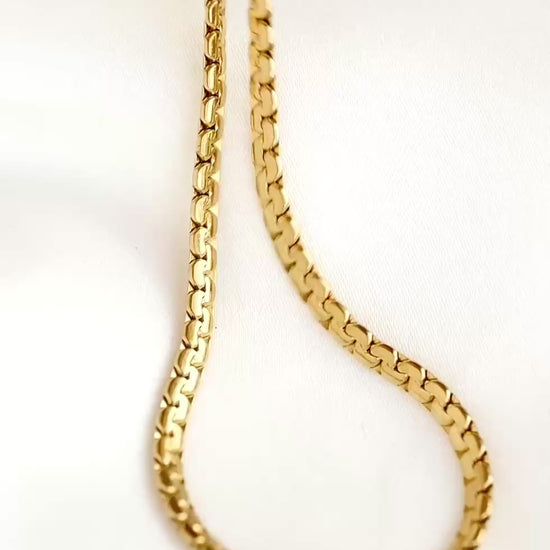 Gold snake bone chain on white satin fabric, the links reflecting light as the chain moves.