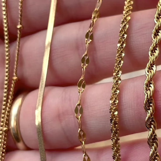 Gold layering chain bracelets in hand with chains reflecting light as the hand moves.