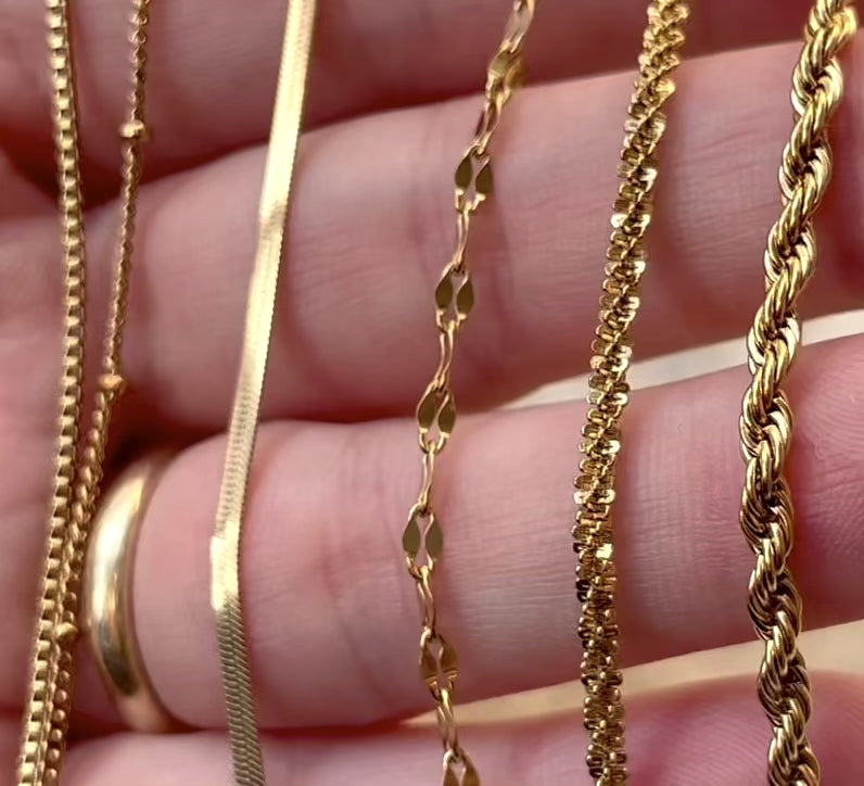 Gold layering chain bracelets in hand with chains reflecting light as the hand moves.
