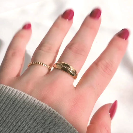 Gold pyramid ring stacked with a chunky dome ring on a hand with burgundy nail polish with rings reflecting light as the hand moves