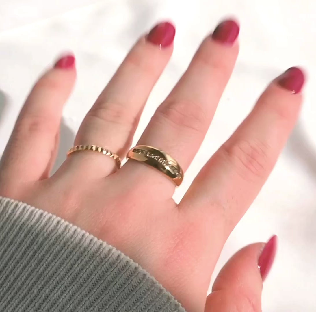 Gold pyramid ring stacked with a chunky dome ring on a hand with burgundy nail polish with rings reflecting light as the hand moves