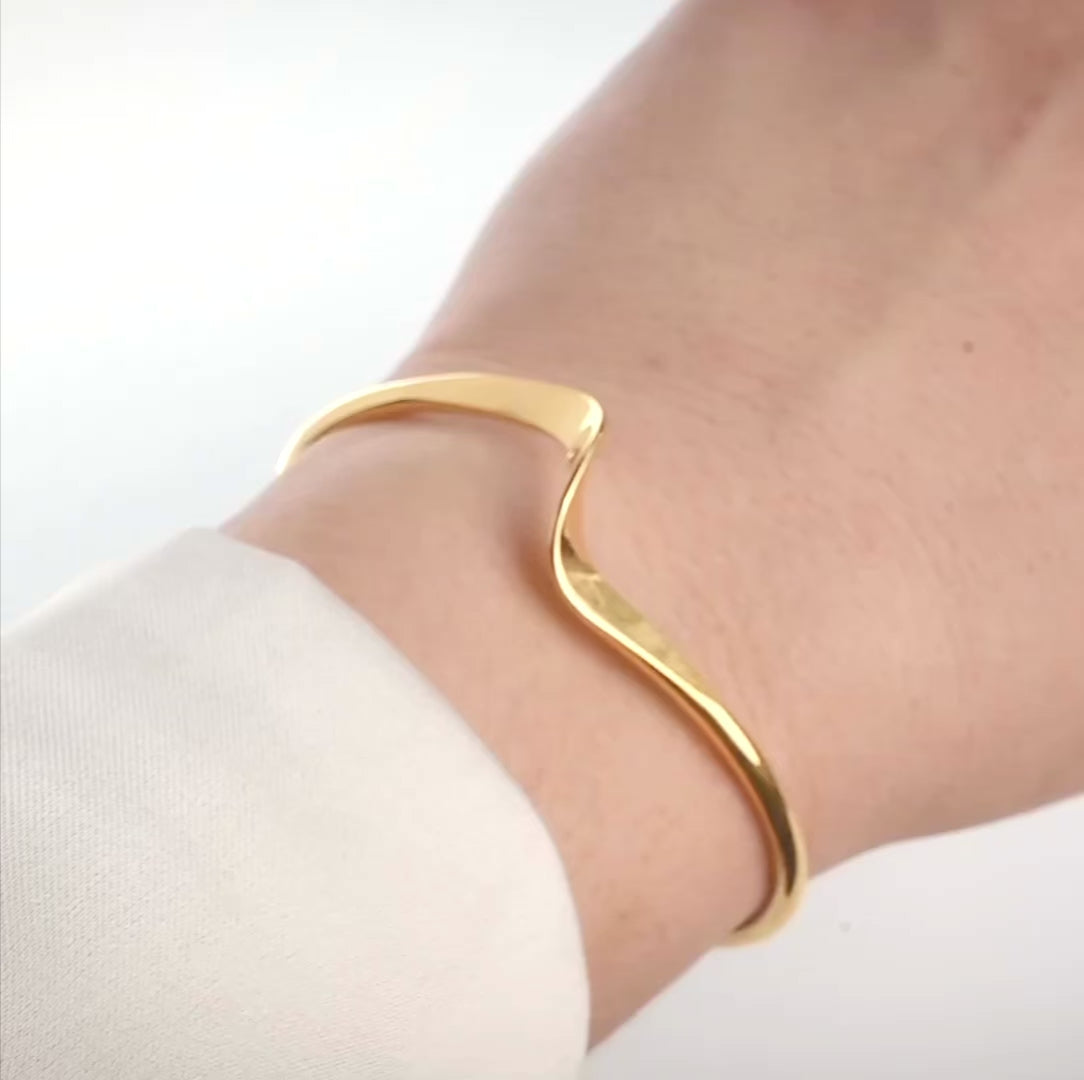 Stainless steel gold cuff bracelet with a unique twist in the front on a wrist, reflecting light as model turns their wrist.