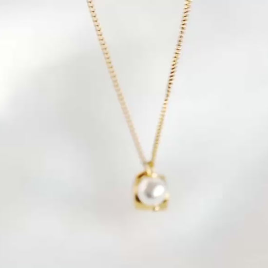A delicate gold chain necklace on white background, featuring a small gold coffee cup charm with a white pearl accent, moving an reflecting as it catches light