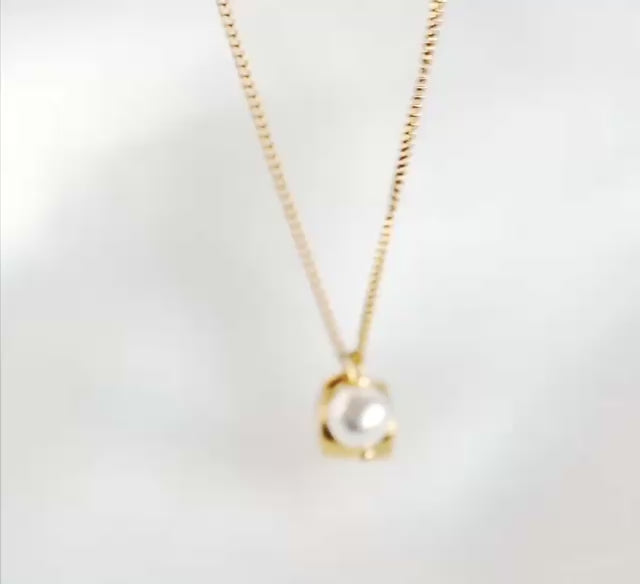 A delicate gold chain necklace on white background, featuring a small gold coffee cup charm with a white pearl accent, moving an reflecting as it catches light