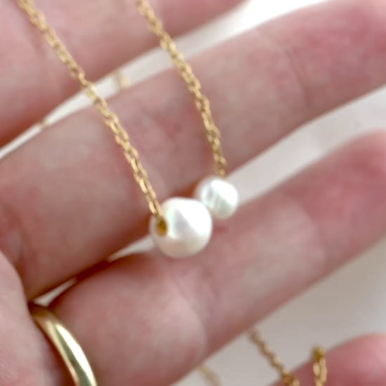 A gold cable chain with one medium and one small baroque pearls shown in hand, with chain links catching light as the hand moves and camera changes angle suring the video