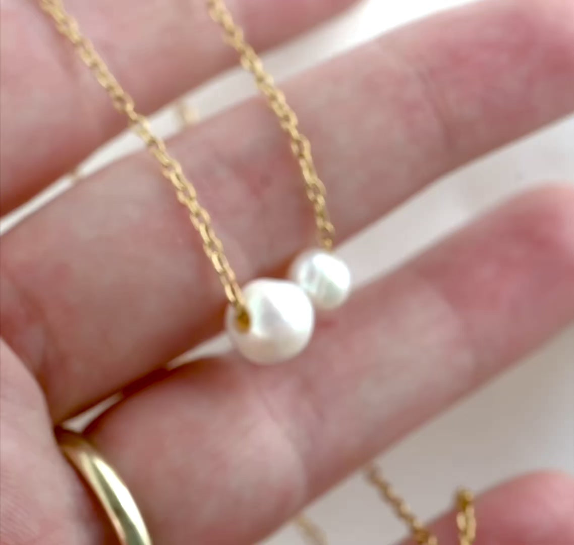 A gold cable chain with one medium and one small baroque pearls shown in hand, with chain links catching light as the hand moves and camera changes angle suring the video