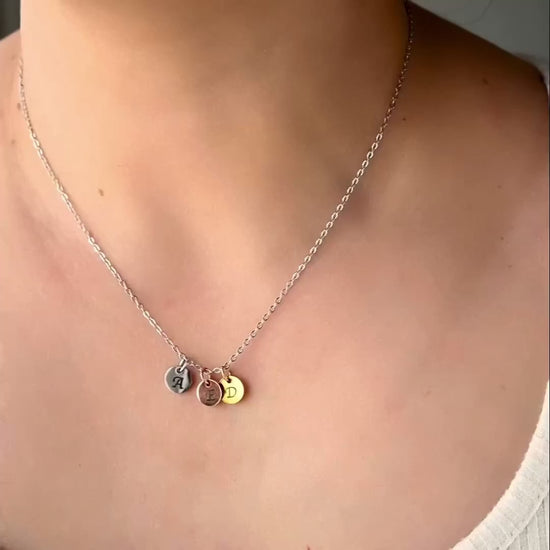 Three tone necklace with a silver cable chain and gold, silver and rose gold letter charms reflecting light as the model moves.