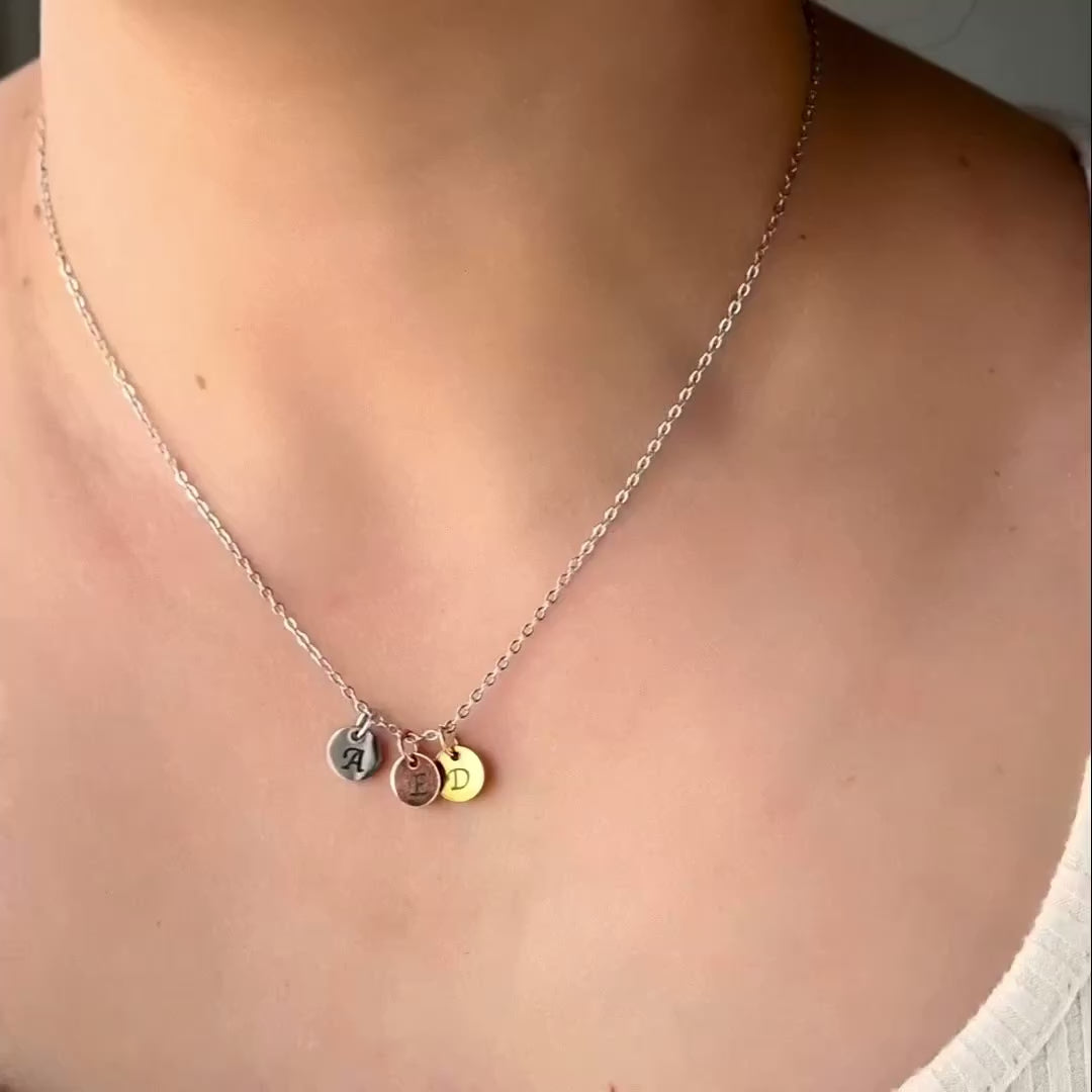Three tone necklace with a silver cable chain and gold, silver and rose gold letter charms reflecting light as the model moves.