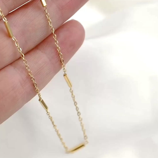 Sleek gold bar station chain in hand, the bars reflecting light as the chain moves