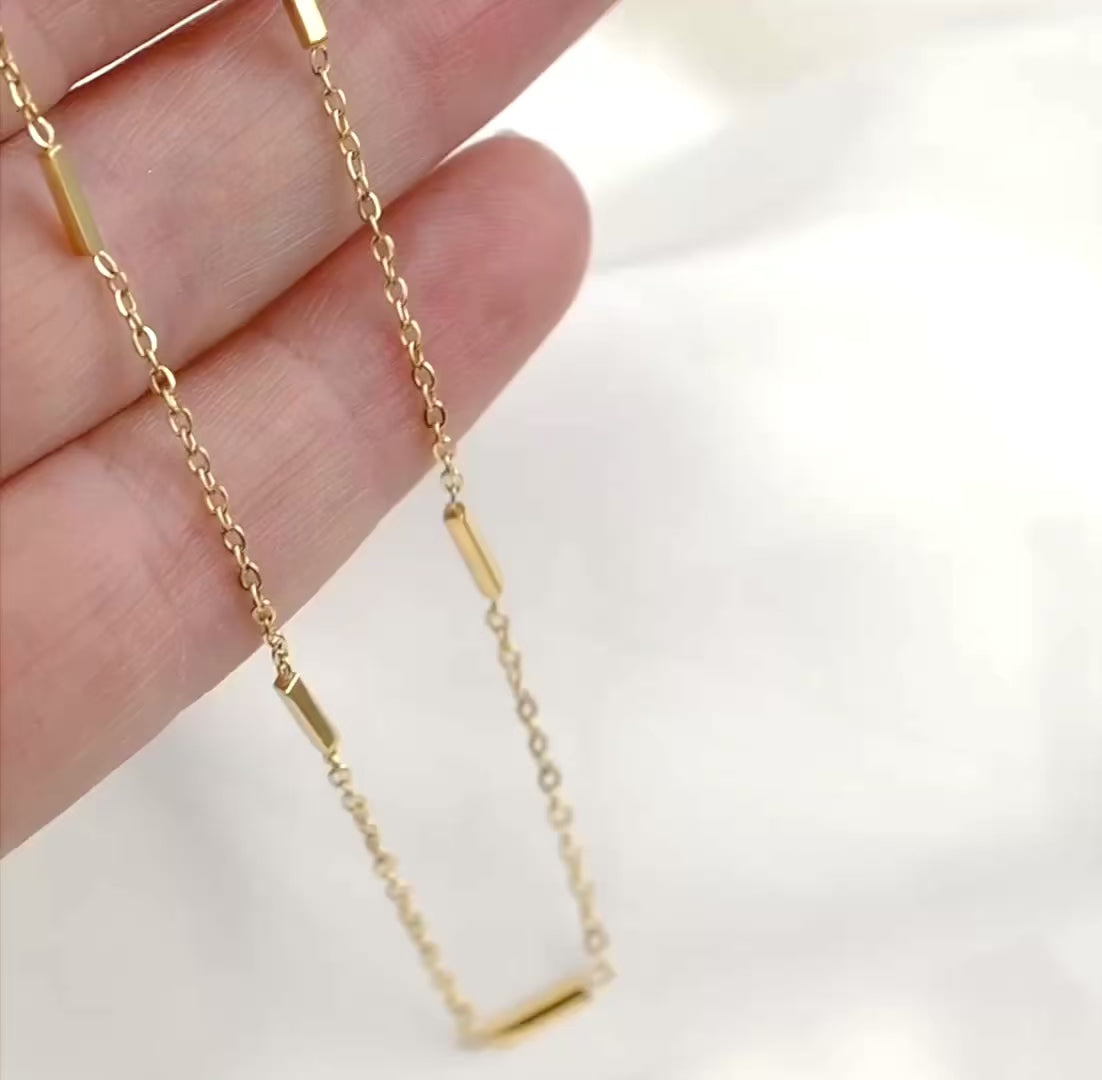 Sleek gold bar station chain in hand, the bars reflecting light as the chain moves