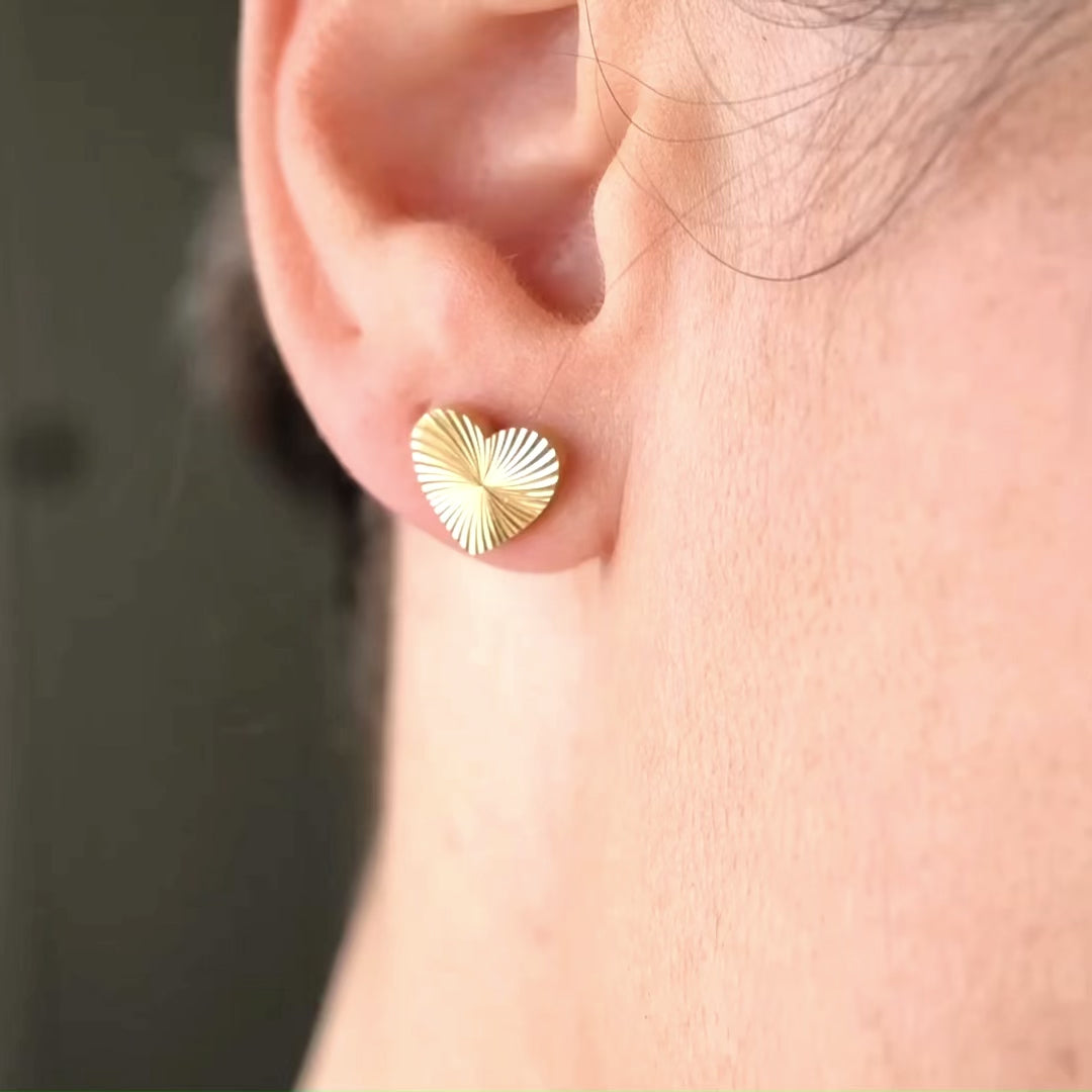 Heart stud earrings on a person with ribbed grooves reflecting light as the person turns.
