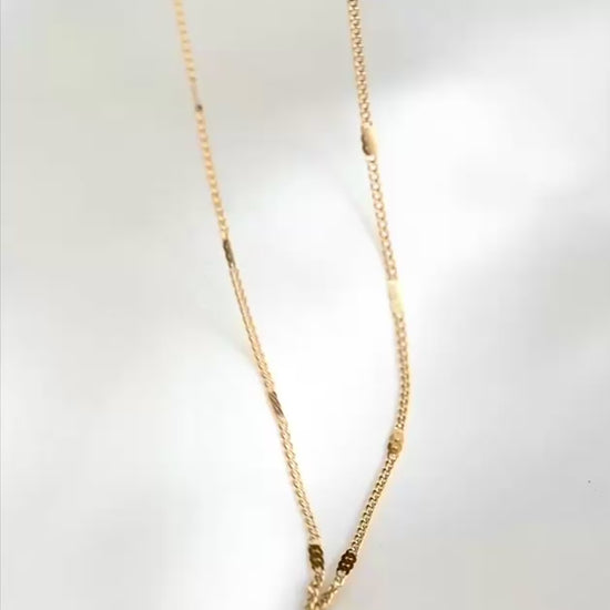 Ultra thin gold curb chain with flat rectangular beads stationed along, reflecting light as the chain moves.